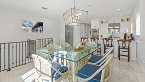 A modern kitchen with white cabinets, stainless steel appliances, and a glass dining table with blue cushioned chairs.
