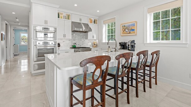 A modern kitchen with white cabinetry, stainless steel appliances, and a large island with bar stools.