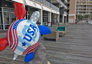Uma grande tartaruga inflável com a inscrição 'USA', colocada em um deck de madeira em frente a um hotel com área de estar externa e uma placa.