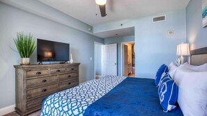 Quarto com cama, penteadeira, televisão e porta que dá para outro cômodo.