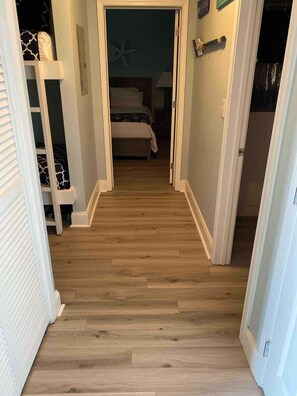 A narrow hallway with wooden flooring leading to a bedroom with a bed and a starfish decoration on the wall. - 18 to Book! Breathtaking Beach Gulf View Sleeps 6 (Panama City Beach)