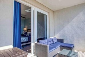 A balcony with wicker furniture, a blue curtain, and a glimpse of a room with a bed and lamp. - 18 to Book! Breathtaking Beach Gulf View Sleeps 6 (Panama City Beach)