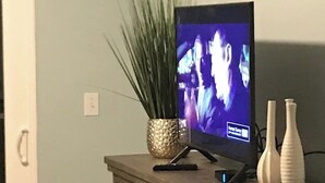 Una televisió sobre una petita estanteria de fusta amb calaixos, una planta decorativa i dos vasetes.