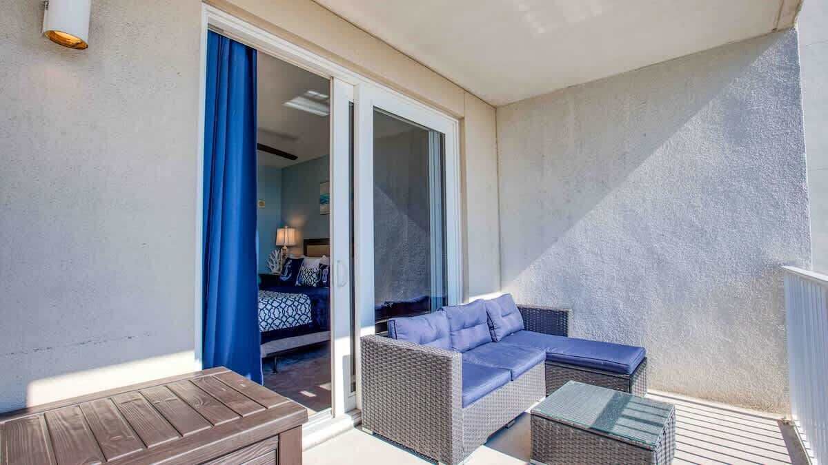 A balcony with a wicker sofa, a wooden table, and a glass partition.
