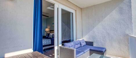 A balcony with a wicker sofa, a wooden table, and a glass partition.