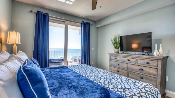 Un dormitorio con cama, cómoda, televisor y balcón con cortinas.