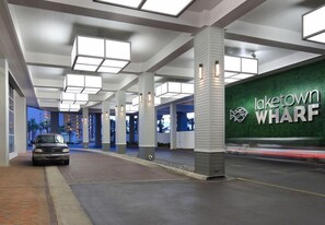 A modern hotel lobby with a car parked in front, a green wall with the hotel name, and a ceiling with square light fixtures.