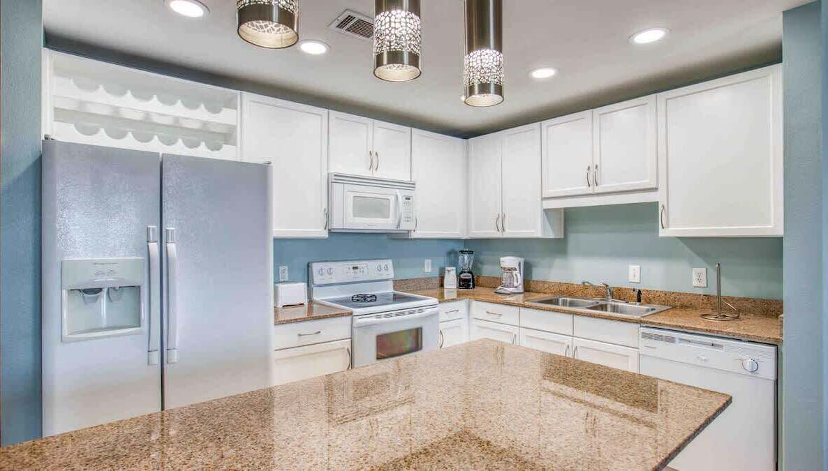 Una cocina moderna con armarios blancos, encimeras de granito, microondas integrado, estufa y cafetera.
