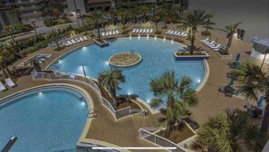 Uma grande piscina coberta com várias pistas de natação, rodeada por palmeiras e espreguiçadeiras.