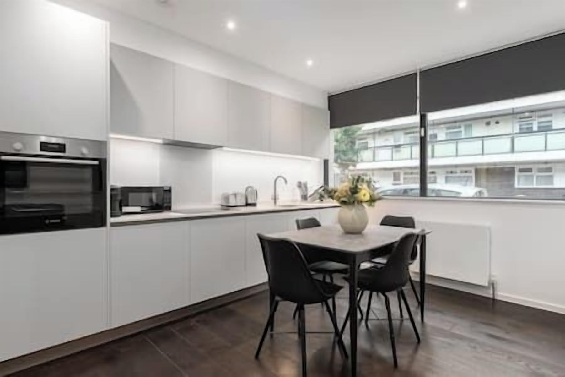 A modern kitchen with white cabinets, a built-in oven, and a dining area with a table and chairs.