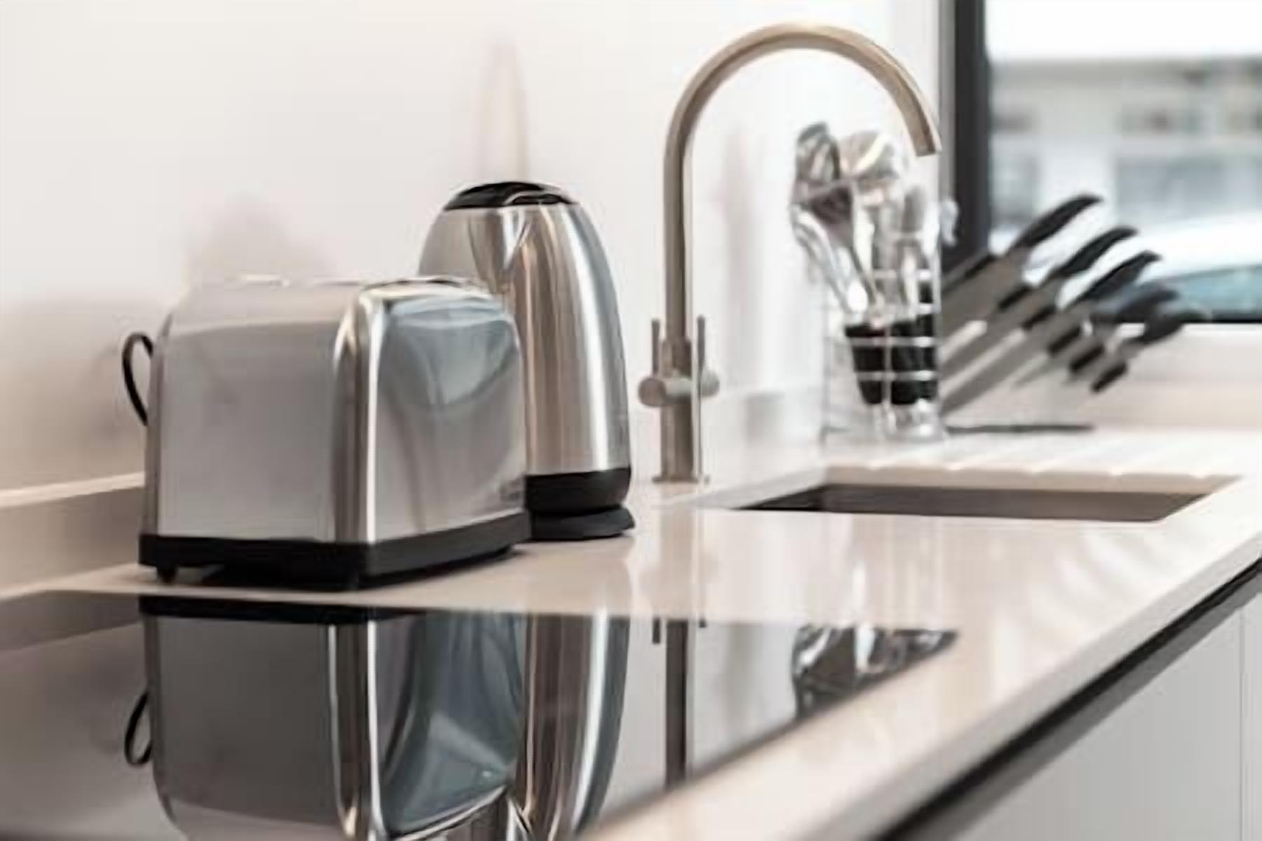 A modern kitchen with a stainless steel toaster, a kettle, and a faucet.