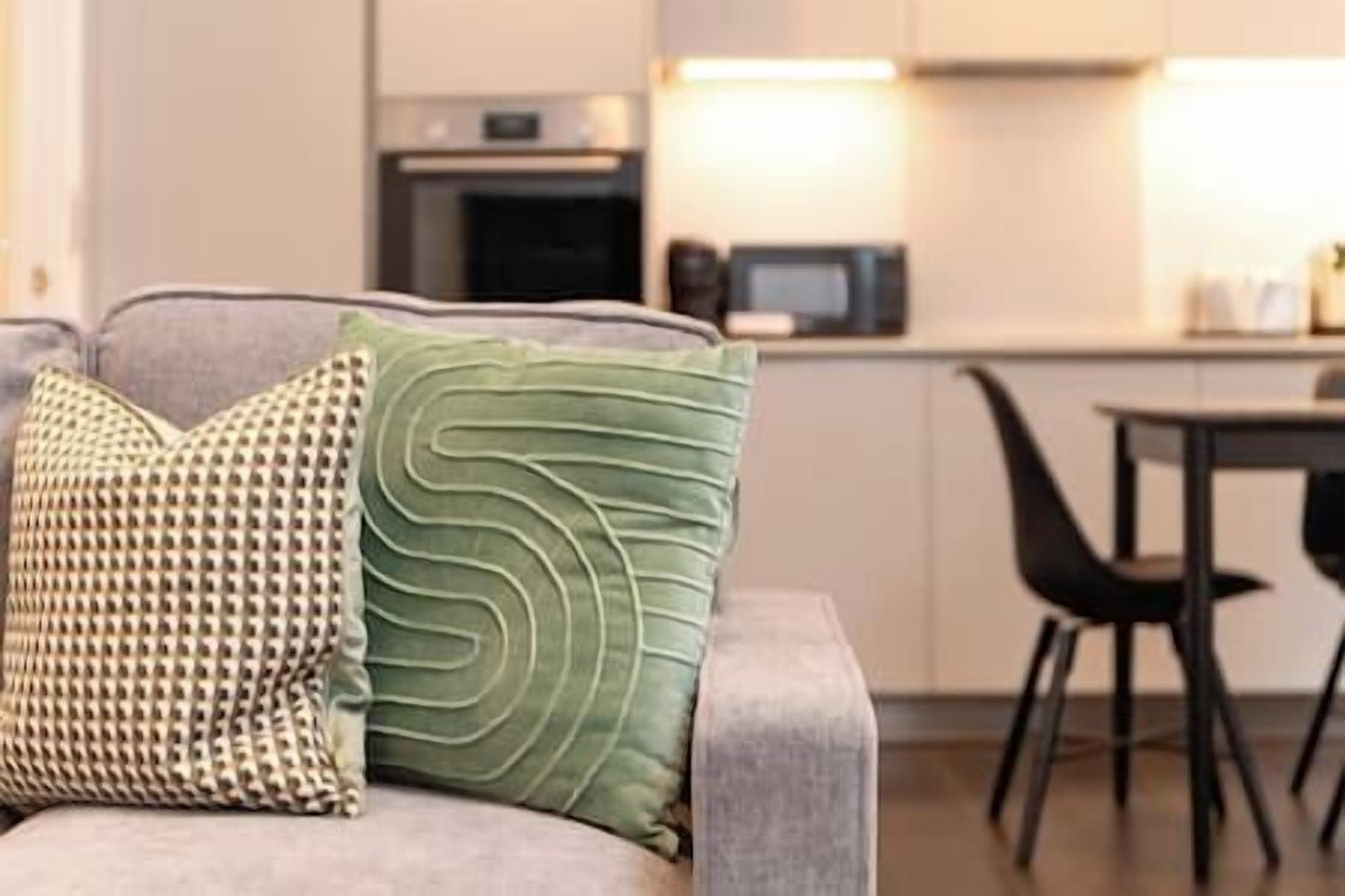 A modern living room with a grey sofa, a patterned pillow, and a green pillow.