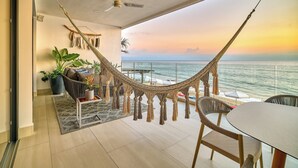 Un balcon avec un hamac, un coin salon et une vue sur l’océan au coucher du soleil.
