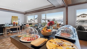 A breakfast buffet with various food items and a view of mountains through large windows. - Crans Montana Suites (Crans-Montana)