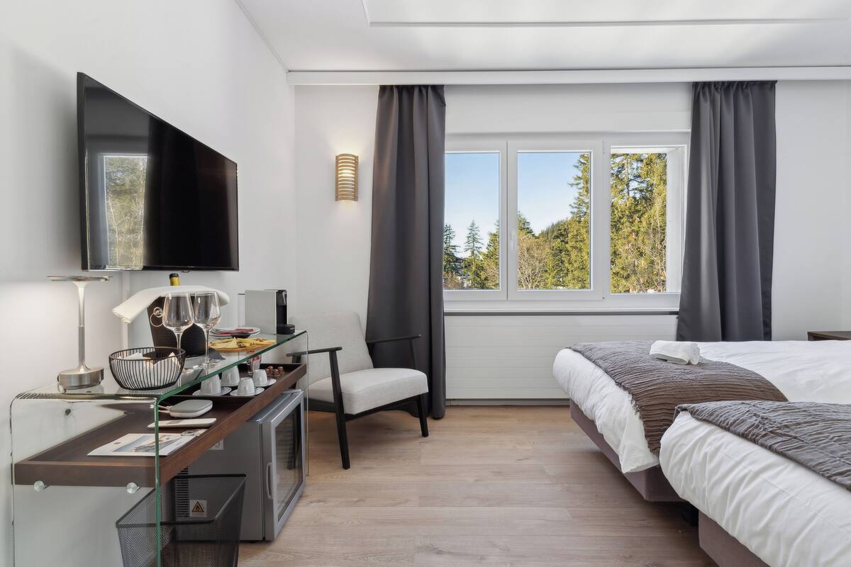 Una camera d'albergo moderna con un letto, una scrivania con un computer, una TV e una finestra con tende.
