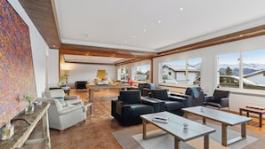 A spacious living area with a large painting, modern furniture, and a view of mountains through large windows. - Crans Montana Suites (Crans-Montana)