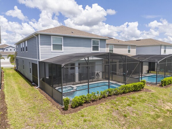 A residential house with a backyard swimming pool covered by a large, enclosed screen structure.