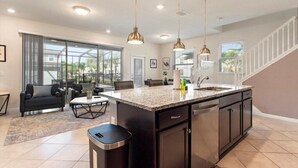 Une cuisine moderne dotée d’un îlot central, de luminaires suspendus et offrant une vue sur l’extérieur.