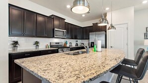 Une cuisine moderne avec des meubles de couleur sombre, des plans de travail en granit, des appareils électroménagers en acier inoxydable et des luminaires suspendus.