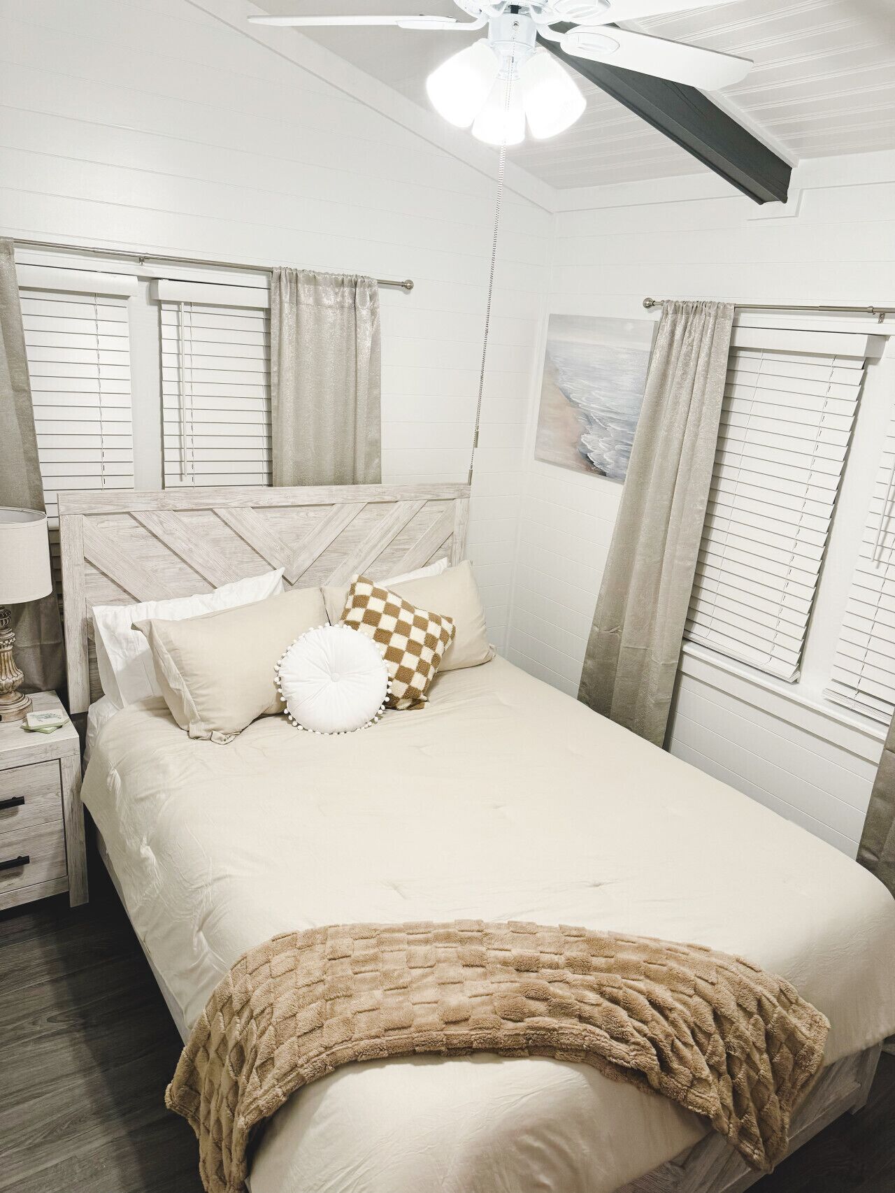 A bedroom with a bed, a nightstand, a lamp, a ceiling fan, and a window with blinds.