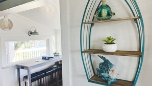 A kitchen with a white countertop, a wooden table, and a wall-mounted shelf with decorative items. - Ultimate Fishing Retreat: Spacious 3BR Bolivar Island Home with Dock & Cleaning Stations - Sleeps 12! (Bolivar Peninsula)
