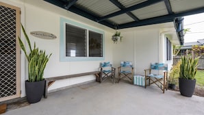 A covered porch with a bench, two chairs with beach-themed cushions, and potted plants.