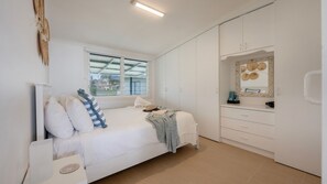 A bedroom with a bed, a window, a wardrobe, and a bathroom with a mirror. - Driftaway- Absolute Beach Front- Stone Real Estate Yamba (Brooms Head)