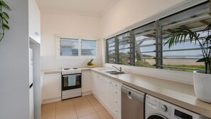 A modern kitchen with a built-in oven, a dishwasher, and a window with a view of the beach. - Driftaway- Absolute Beach Front- Stone Real Estate Yamba (Brooms Head)