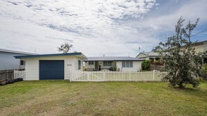 A single-story house with a garage, a fenced yard, and a tree.