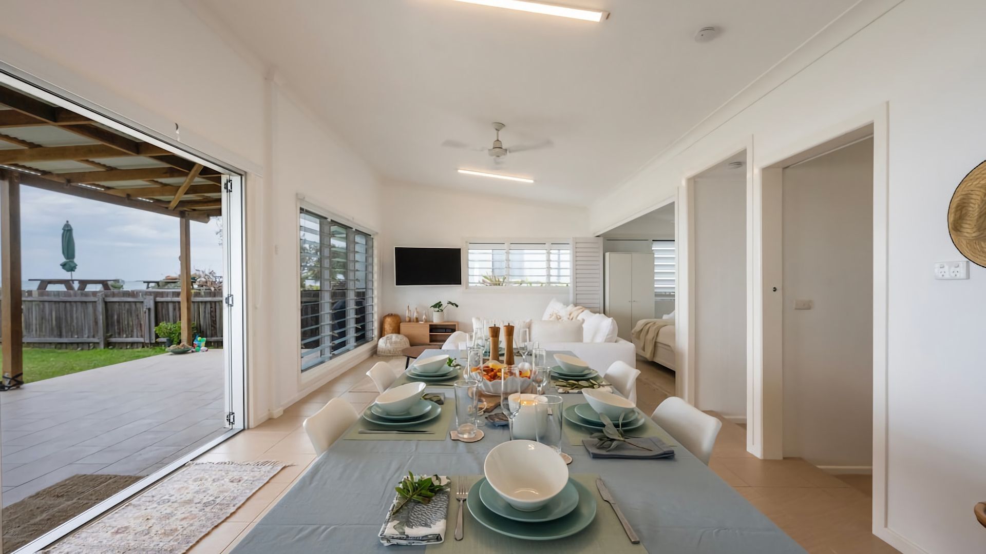 A spacious dining area with a table set for a meal, a ceiling fan, and a view of the outdoors.