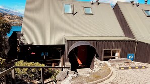 Un bâtiment doté d’un toit en tôle ondulée, d’une porte en bois portant le numéro 12, et dont on aperçoit un lac au loin.