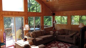 A wooden cabin interior with a large window, a ceiling fan, and a red patterned rug.
