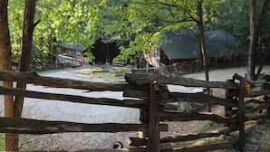 A rustic wooden fence in a wooded area with a gravel path and a building in the background.