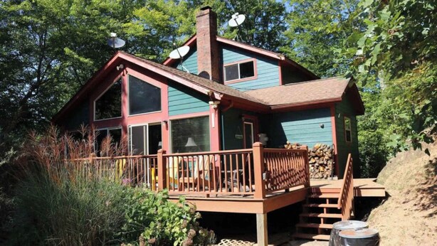 A two-story cabin with a deck, satellite dishes, and a chimney.