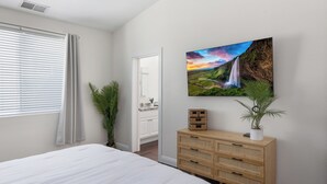 Ein Schlafzimmer mit einem Bett, einem Schminktisch, einer Zimmerpflanze und einem Bild eines Wasserfalls.