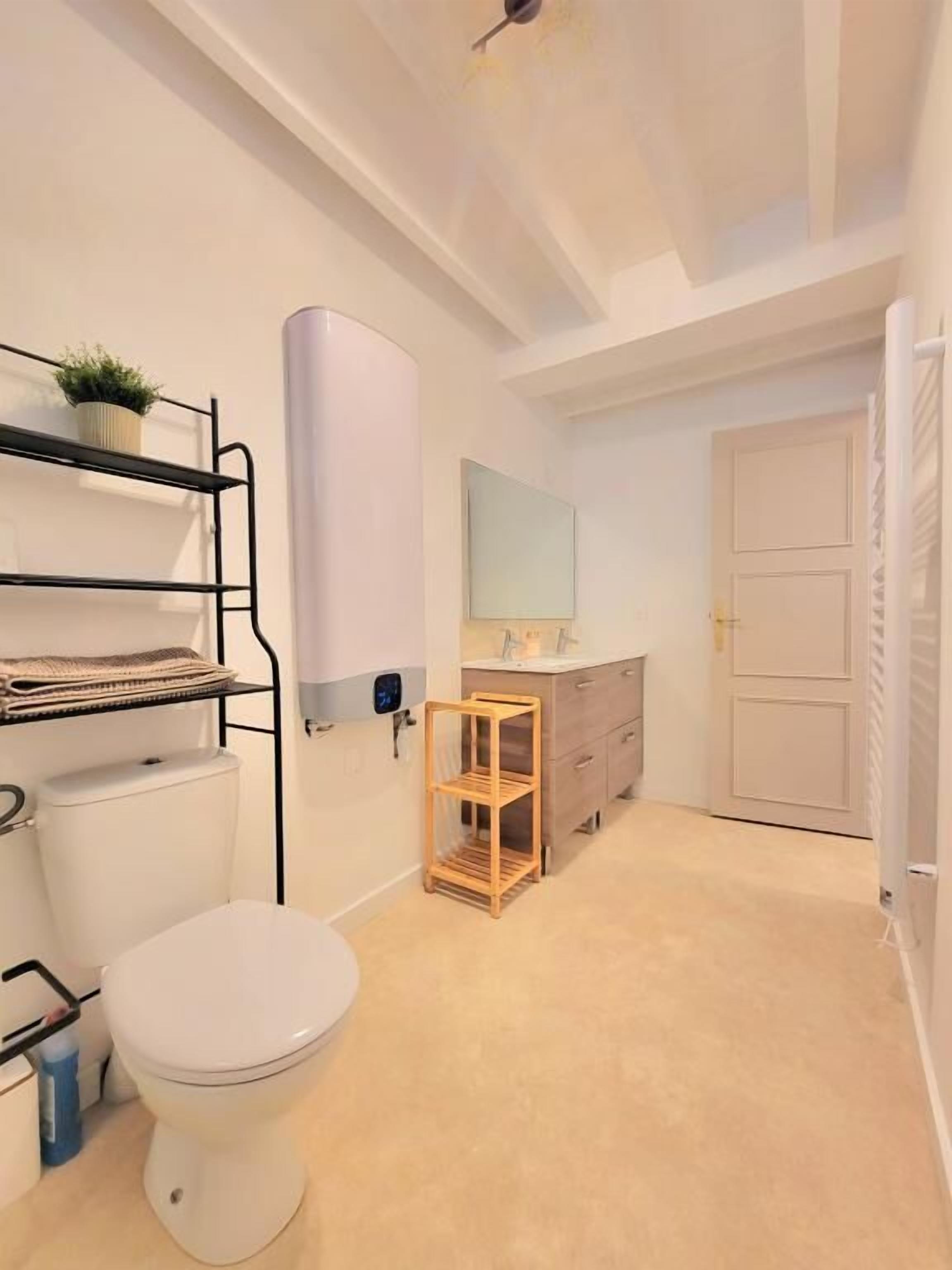 Une petite salle de bain comprenant des toilettes, une étagère avec des serviettes, un étendoir en bois et un meuble-lavabo avec un miroir.