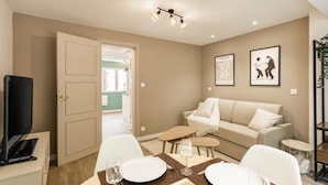 A modern living room with a sofa, a dining table set for two, and a television on a stand.