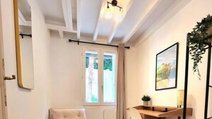 A modern room with a wooden floor, a sofa, a desk with a chair, a mirror, and a window with curtains.