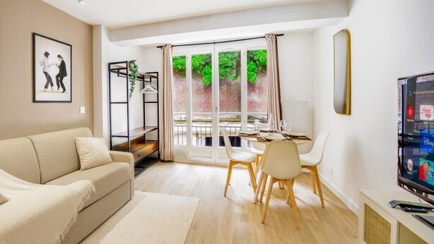 A modern living room with a sofa, dining table, chairs, a TV, and a sliding glass door leading to an outdoor area.