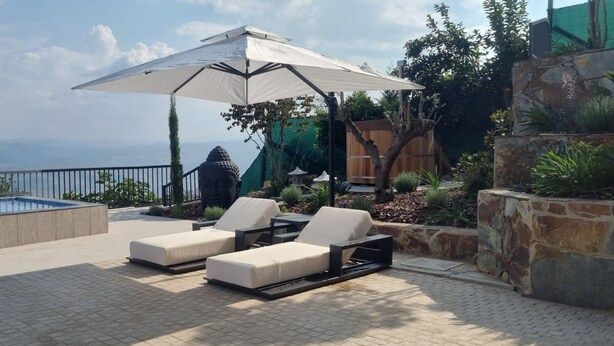 A poolside area with lounge chairs and a large umbrella, surrounded by plants and a view of distant mountains. - Quinta de Raj (Peso da Régua)