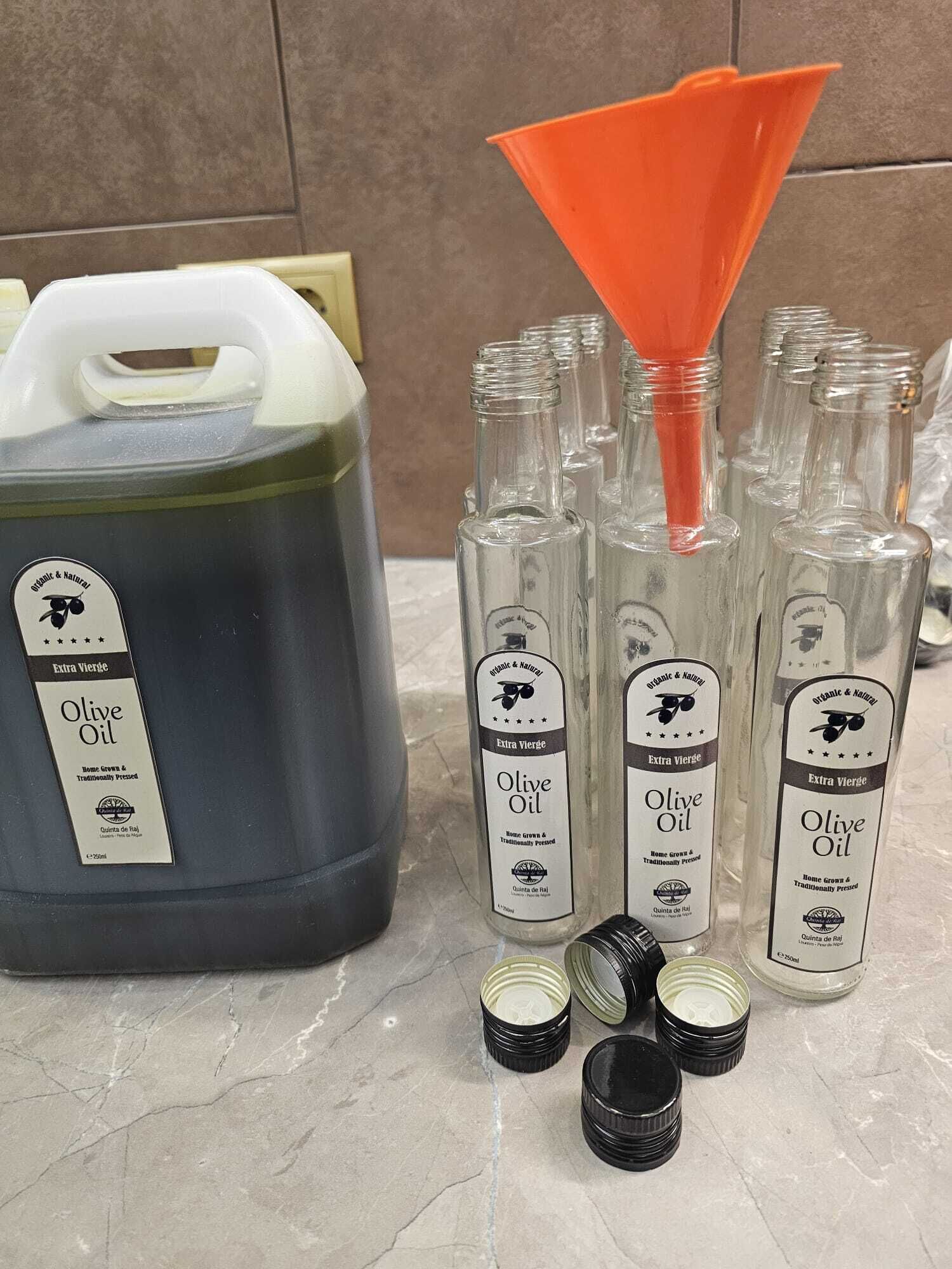 A large container of olive oil with several smaller bottles and empty containers on a marble surface.