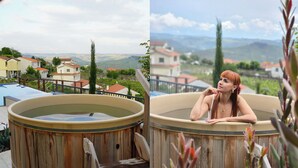 Una vasca idromassaggio in legno con vista su case e vigneti sullo sfondo.