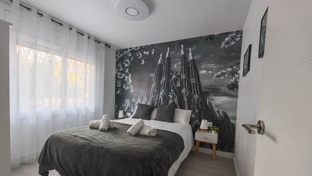 Un dormitorio con una cama, una mesita de noche, un mural en la pared y una ventana con cortinas.