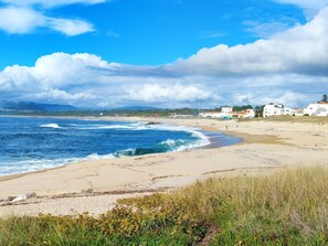 A beach with waves, a sandy shore, and buildings in the background. - Seren Água | Beach | Moledo | 2 minutes walk from the beach (Moledo)