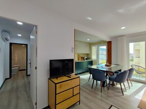 A modern living room with a flat-screen TV on a wooden cabinet, a dining area with a glass table and four chairs, and a kitchen with a microwave and cabinets. - Seren Água | Beach | Moledo | 2 minutes walk from the beach (Moledo)