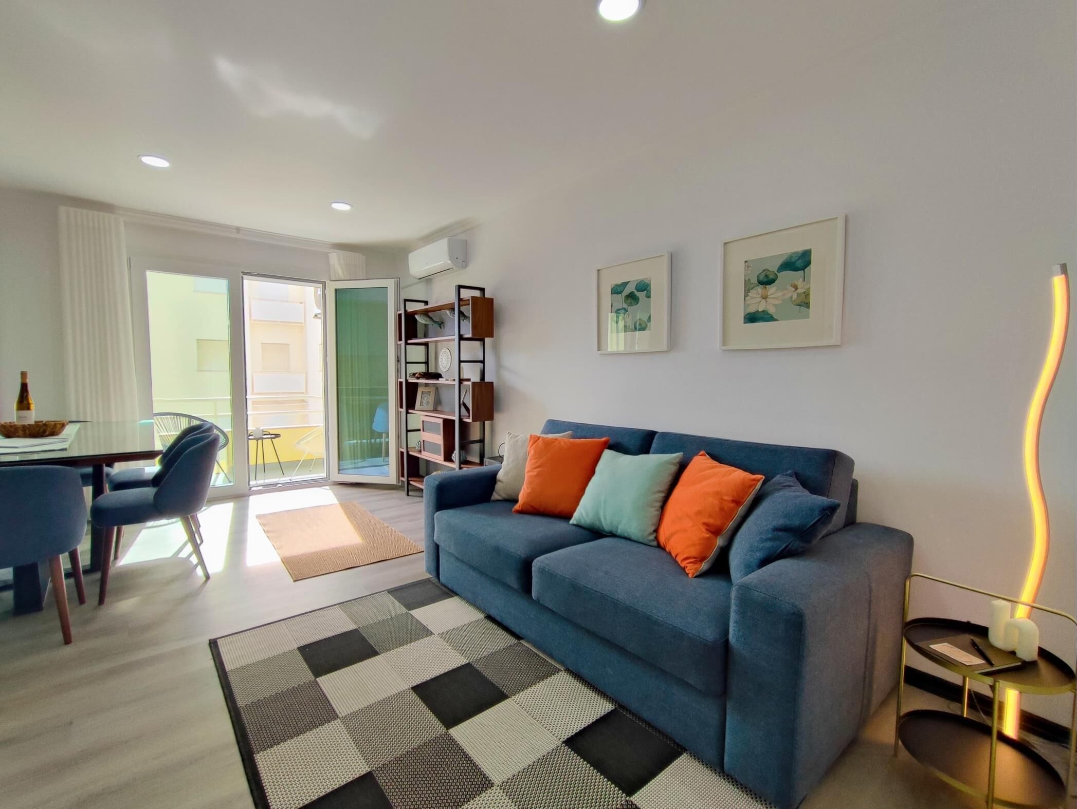 Una sala de estar moderna con un sofá azul, un tapete blanco y negro, y un comedor con una mesa y sillas.