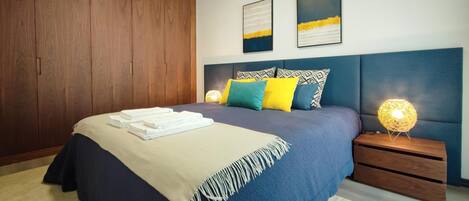 A modern bedroom with a large bed, a wooden wardrobe, and two wall-mounted artworks.