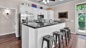 A modern kitchen with white cabinetry, stainless steel appliances, a glass island with bar stools, and a ceiling fan.