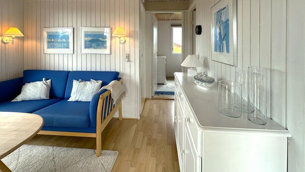 Una habitación con un sofá azul, una silla de madera, un aparador blanco con cristalería y cuadros en la pared.