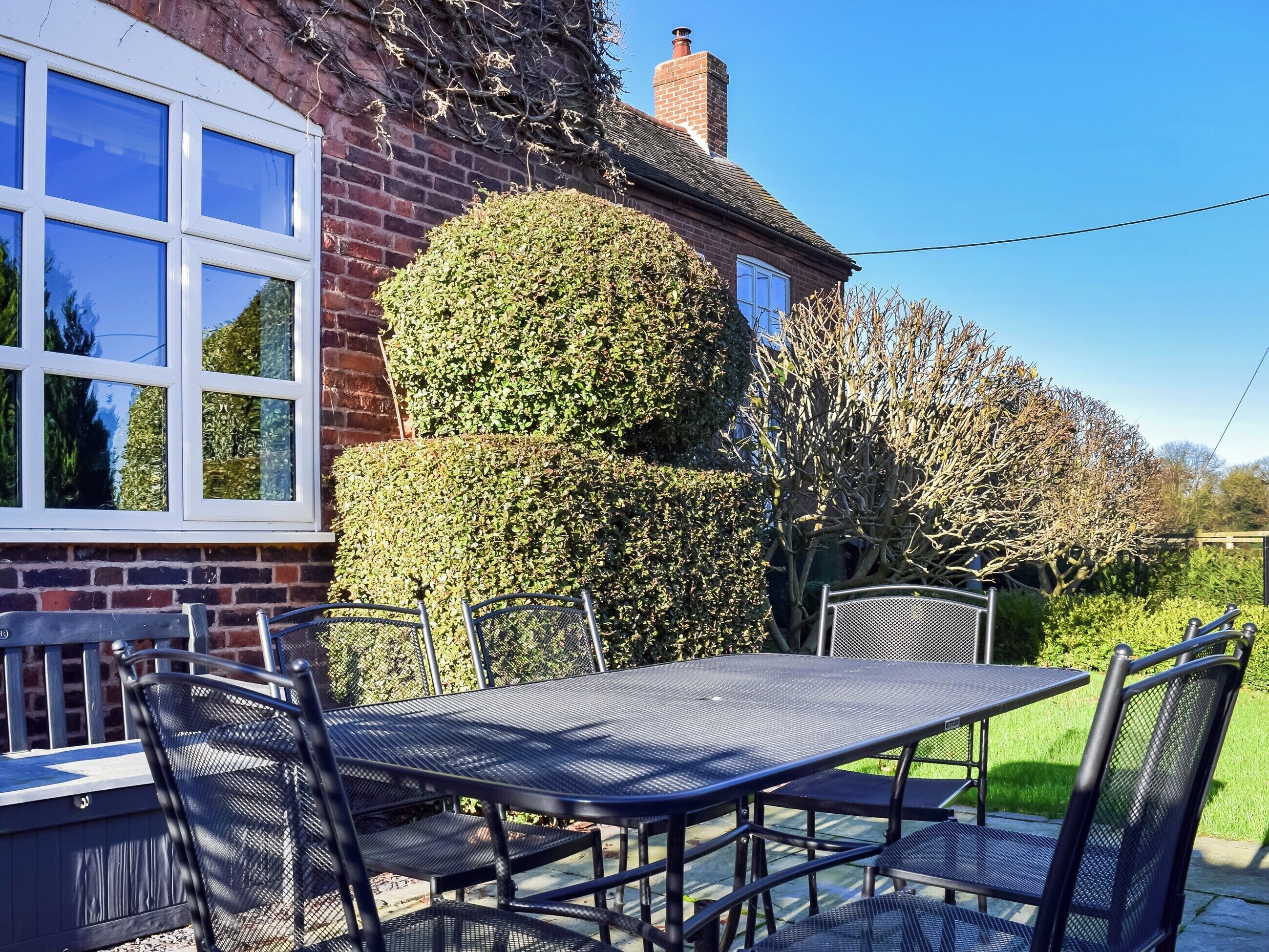 A patio with a table and chairs, a brick house, and a well-maintained hedge.